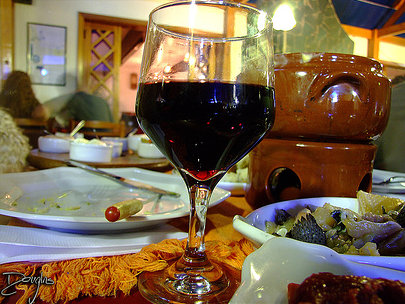 Taça de vinho com fondue ao fundo.