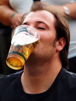 Homem segurando um copo de cerveja com a boca
