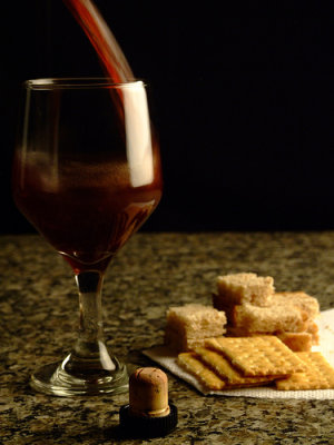 Taça de vinho com biscoitos ao fundo.