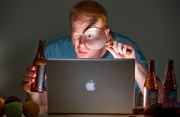 Homem com lente olhando pra um Laptop e com cerveja na mão