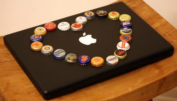 Macbook preto com tampinhas de cerveja em cima formando um coração