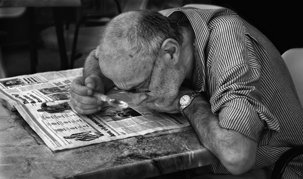 Idoso lendo jornal com lente