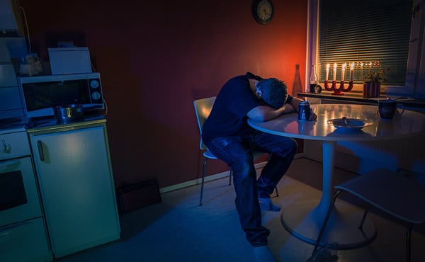 Homem sentado numa mesa chorando e bebendo cerveja