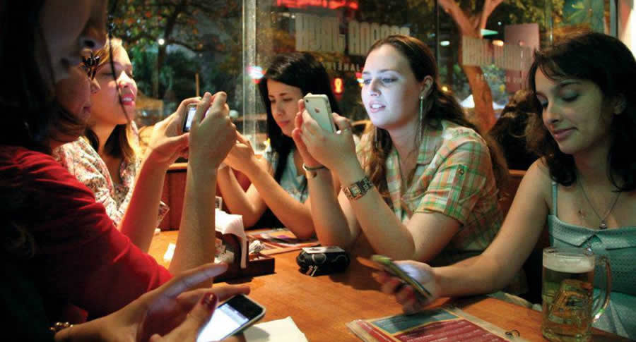 Mulheres sentadas numa mesa de bar mexendo no celular