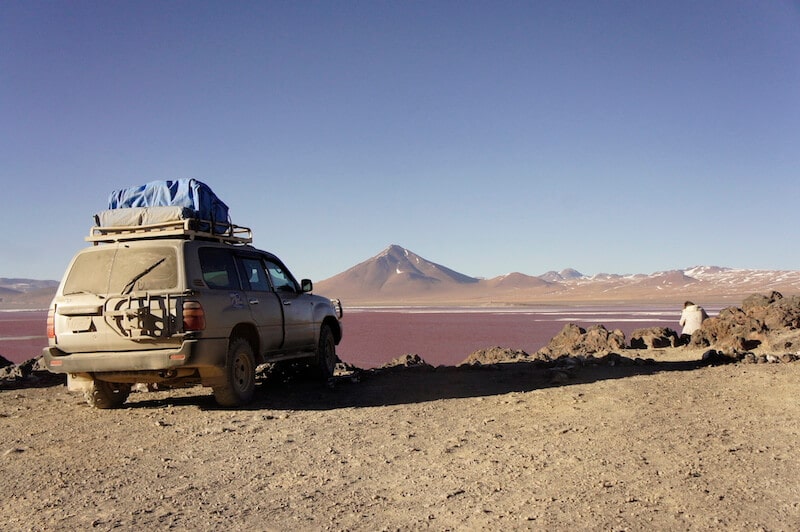 carro 4x4 com montanha ao fundo e lagoa vermelha no mochilão